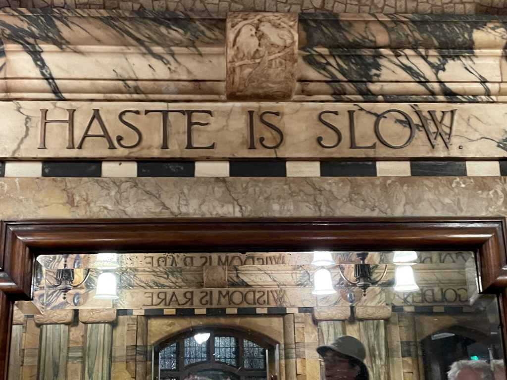 An elaborate script on an archway in a British pub reads, "Haste is Slow."
